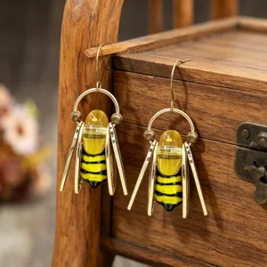 Boucles abeilles rayées jaune et noir, ailes dorées, suspendues devant un coffret en bois