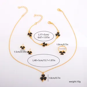 Flat lay of gold-tone jewelry with black enamel clover motifs: necklace, bracelet, earrings and ring
