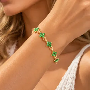 Close-up of a wrist wearing a gold-tone bracelet with green crystal four-leaf clover charms