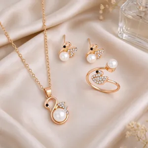 Flat lay of gold-tone swan jewelry with pearl and crystal accents on a soft satin background