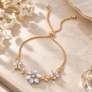 Close-up of clear crystal flower and branch details on a gold-tone bracelet, laid on stone