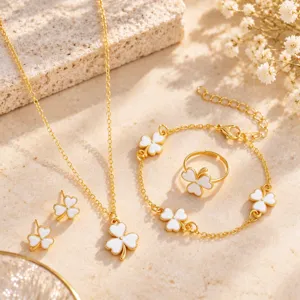 Flat lay of gold-tone jewelry with white enamel four-leaf clover charms on a warm stone surface
