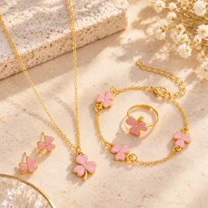 Gold-tone chains and ring with pink enamel clover charms arranged on a warm stone surface