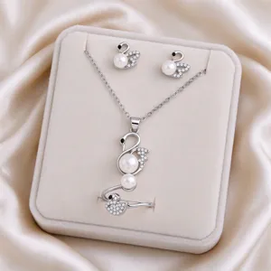 Silver swan-shaped pieces with faux pearls and clear stones arranged on a beige velvet display pad