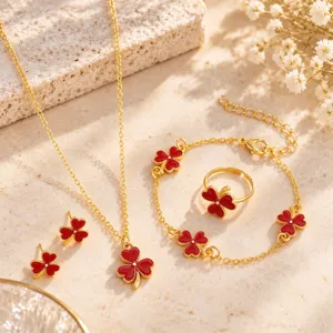 Jewelry set arranged on pale stone, showing red enamel four-leaf clovers on gold-tone pieces