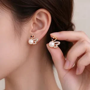 Close-up of gold swan stud earrings with pearl accents and clear stones, worn and held by hand