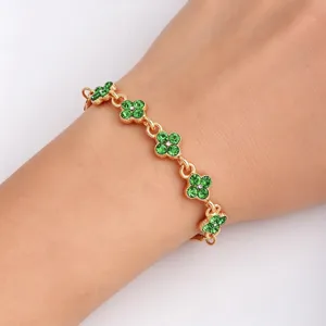 Close-up of a gold-tone bracelet with green clover charms and white accents worn on the wrist