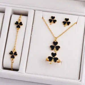 Four black clover jewelry pieces with gold edging arranged in a white velvet display box