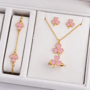 Pink enamel clover pieces from a gold-tone jewelry set arranged in a white velvet box