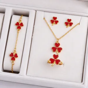 Red enamel four-leaf clover jewelry pieces with beaded gold-tone borders arranged in a white box