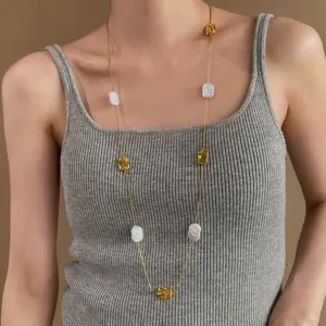 Collana dorata con perline irregolari e perle barocche bianche, indossata su un top grigio a coste
