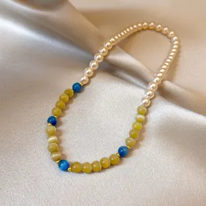Dettaglio di perle bianche effetto perla, gialle e blu con distanziatori dorati su raso morbido
