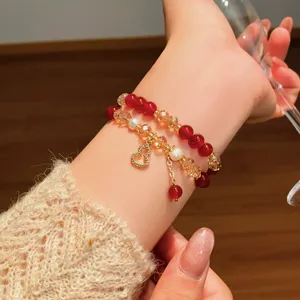 Dettaglio del bracciale al polso con perline rosse, accenti perlati e ciondolo dorato a zucca
