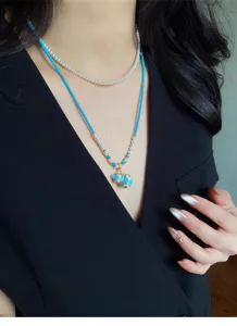 Collana lunga blu con perline e perle sintetiche, indossata con ciondolo smaltato e dettagli dorati