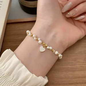 Primo piano di un polso con bracciale dorato, perle bianche e un piccolo ciondolo a forma di cuore