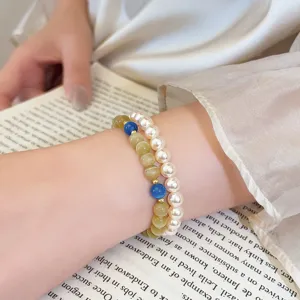 Perle effetto madreperla e perle traslucide giallo-verdi con dettagli blu e dorati indossate al polso