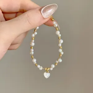 Primo piano di un bracciale di perle con elementi dorati e ciondolo a cuore, su sfondo neutro