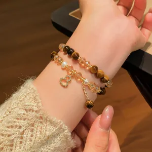 Polso in primo piano con occhio di tigre, cristalli, perle d'acqua dolce e ciondolo a cuore dorato