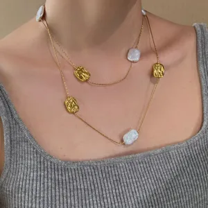 Primo piano di collana dorata a più fili, con perle irregolari e ciondoli quadrati in rilievo