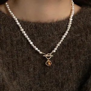 Primo piano di una collana di perle indossata, con chiusura a T dorata e ciondolo in pietra marrone