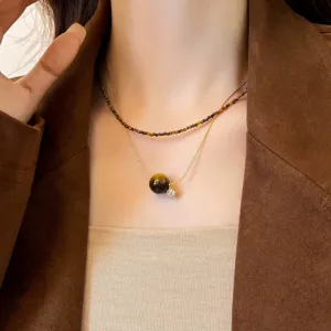 Primo piano di una collana a strati indossata al collo, con perline marroni e pendente dorato