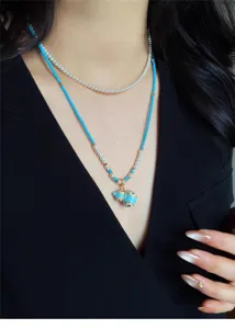 Primo piano di perle bianche e perline blu, con ciondolo smaltato blu e trafori dorati