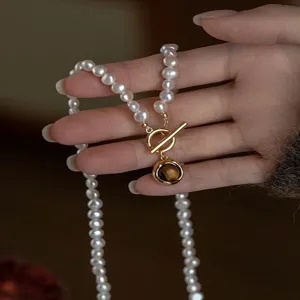 Dettaglio della collana di perle in mano, con chiusura a T dorata e pendente in pietra marrone