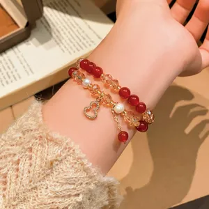 Al polso, bracciali con perline rosse, cristalli champagne, perle bianche e ciondolo dorato
