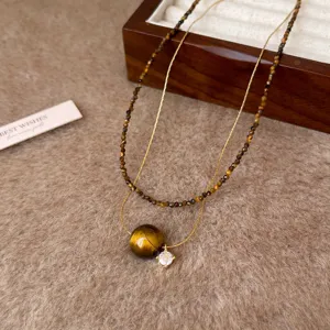 Dettaglio di collana doppia con perle di occhio di tigre sfaccettate, catene dorate e pendente