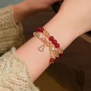 Primo piano di un polso con perline rosse, cristalli color champagne, perle e ciondolo a cuore