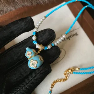 Collana con ciondolo a zucca smaltata blu, fiori dorati, perle bianche e perline turchesi
