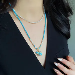 Collana a doppio giro con perle bianche, perline blu e pendente dorato, indossata da una modella