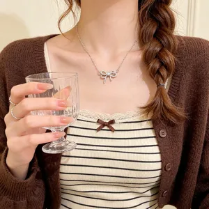 Close-up of a sparkling bow pendant on a fine silver chain, worn at the center of the neck