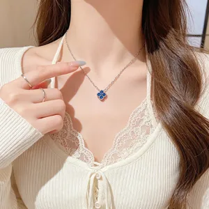 Close-up of a blue four-leaf clover pendant on a silver chain, worn at the neckline in soft light