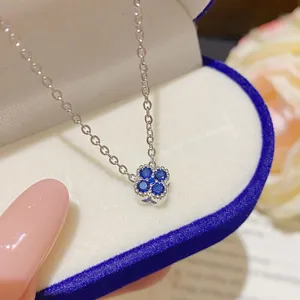 Close-up of a silver-tone four-petal pendant with blue stones in a velvet jewelry box
