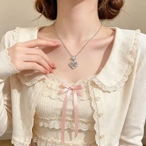 Close-up of a silver-tone heart pendant with a crystal bow, worn on a fine chain against lace