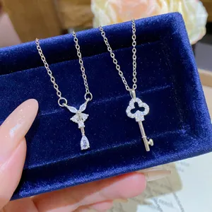 Two silver-tone necklaces with sparkling bow-drop and clover key pendants on a blue velvet box