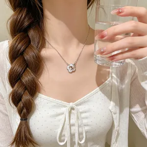 Close-up of a silver chain necklace with a white enamel flower pendant worn at the neckline