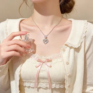 Close-up of a silver-tone heart pendant with a sparkling bow, worn on a delicate chain