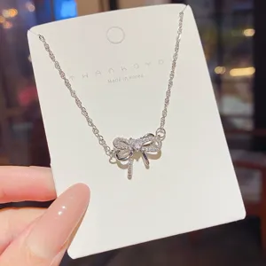Close-up of a sparkling bow pendant with a heart-shaped center, displayed on a white card