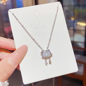 Round clear stone and dangling fishbone charm on a silver-tone pendant, displayed on a white card