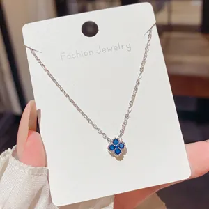 Silver-tone chain with a blue four-leaf clover pendant, displayed on a white jewelry card in hand