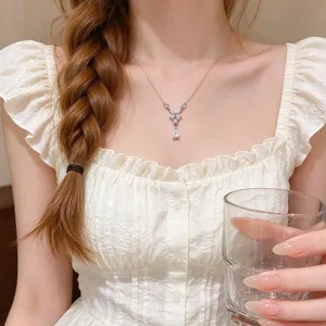 Close-up of a silver necklace worn on a model, with a crystal butterfly and teardrop pendant