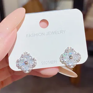 Close-up of two sparkling four-leaf clover earrings with clear stones on a white S925 jewelry card