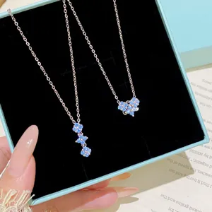 Close-up of two silver-tone chains with blue floral jeweled pendants in a black velvet box