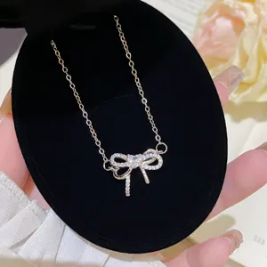 Close-up of a gold-tone chain and crystal-set bow pendant displayed on a black velvet stand