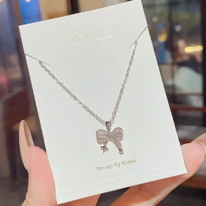 Close-up of a silver-tone bow pendant necklace with sparkling stones, displayed on a white card