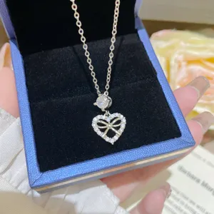 Close-up of a sparkling heart-shaped bow pendant with clear stones in a blue velvet jewelry box