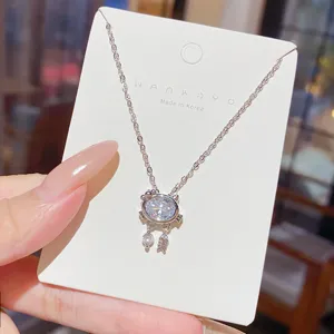 Close-up of a cat-shaped pendant with an oval clear stone and dangling charms on a white card