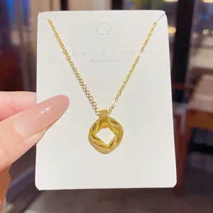 Close-up of a gold-tone fine chain necklace with a woven square pendant displayed on a white card